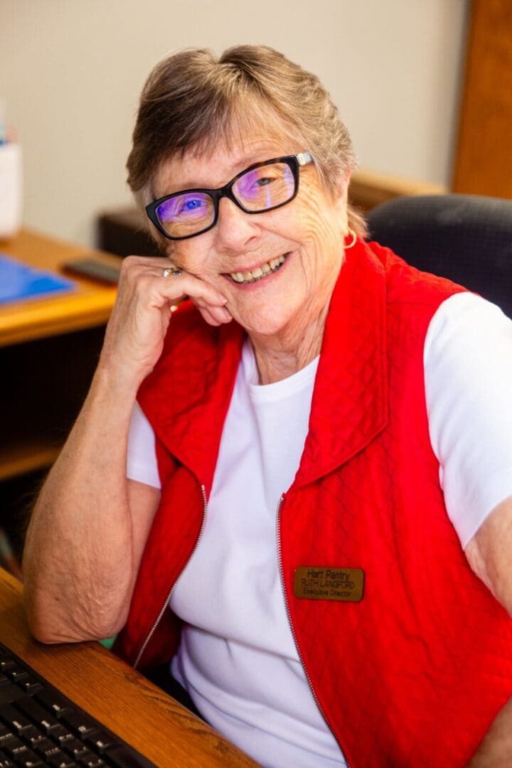 A woman sitting in front of a desk wearing glasses.