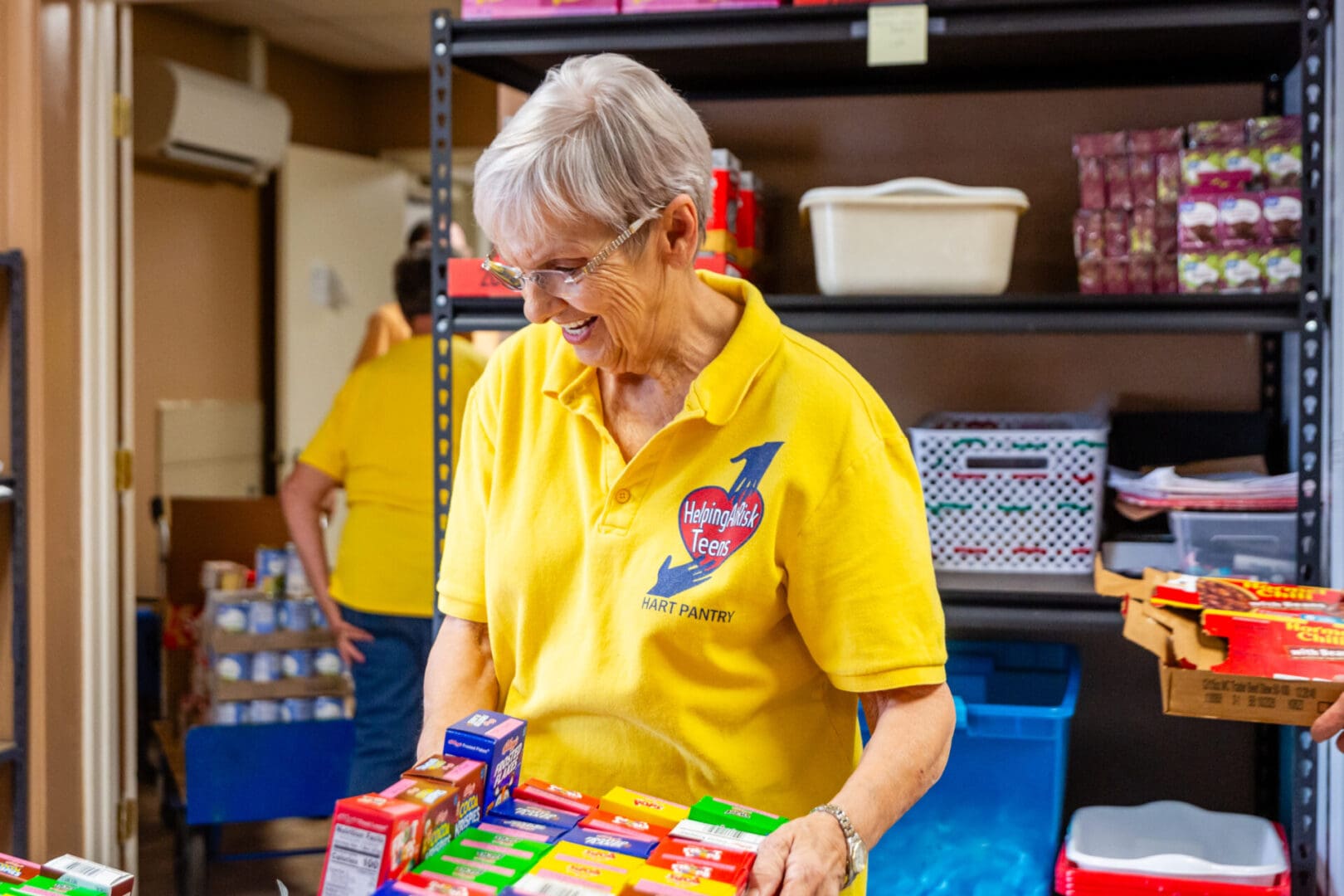 A woman in yellow shirt holding boxes of food.