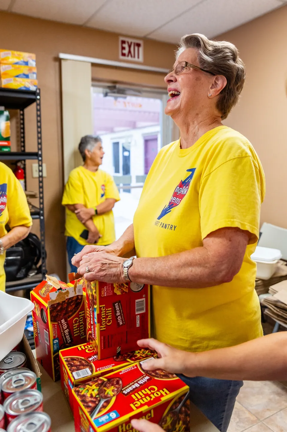A woman in yellow shirt holding onto boxes of food.